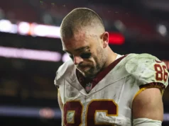 Jake Ertz entra no vestiário, descartado após sofrer uma terrível lesão no joelho durante uma tentativa de captura